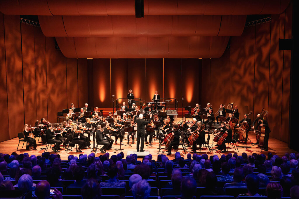 Flevolands Philharmonisch Orkest maakt muziek op een podium met dirigent Hans Welle voor publiek