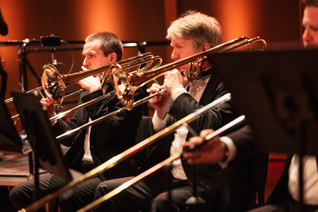 Trombonisten van het Flevolands Philharmonisch Orkest maakt muziek op een podium met dirigent Hans Welle